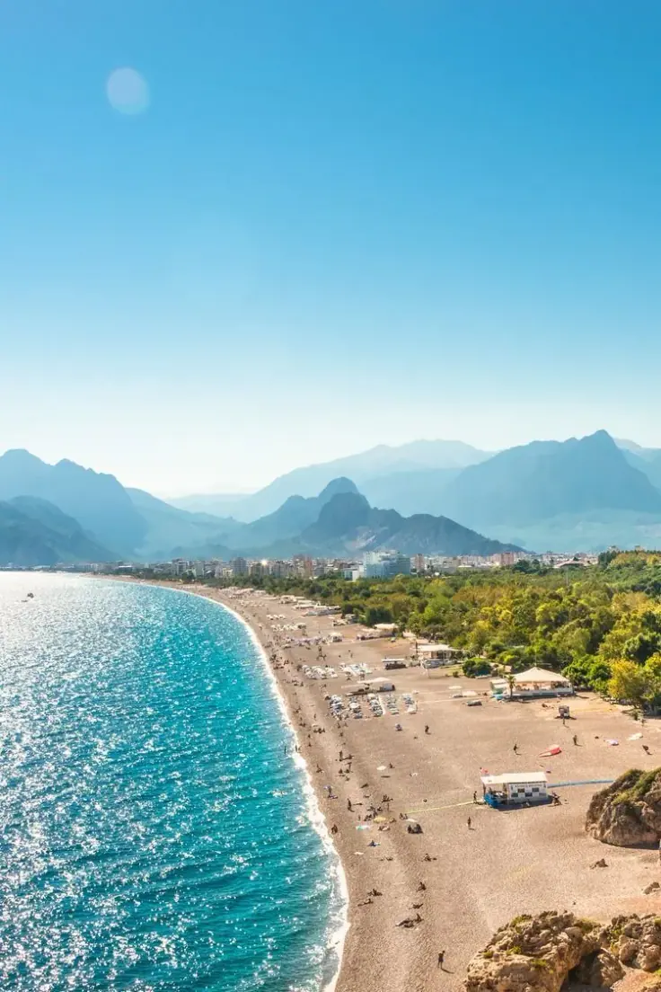 Ein langer, geschwungener Sandstrand unterhalb der Berge an der Mittelmeerküste