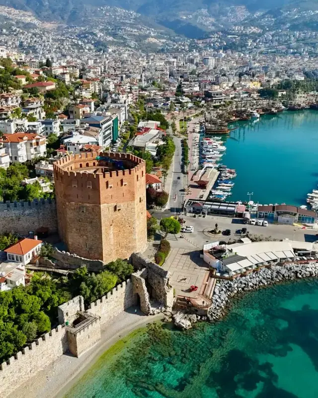 Der Rote Turm und die alten Hafenmauern von Alanya von oben, neben türkisfarbenem Wasser