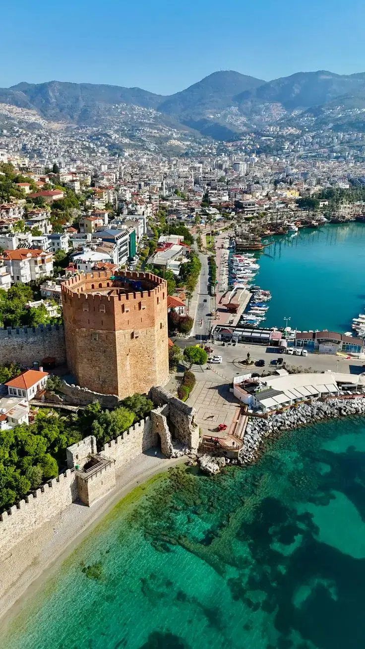 Der Rote Turm und die alten Hafenmauern von Alanya von oben, neben türkisfarbenem Wasser
