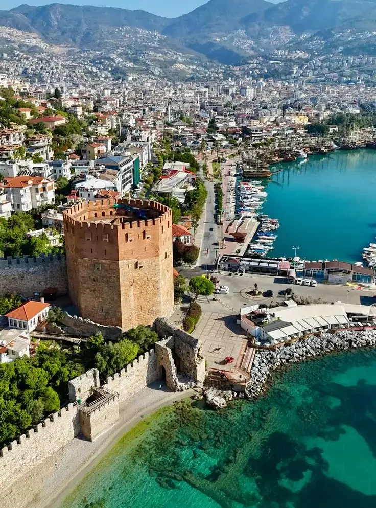 Der Rote Turm und die alten Hafenmauern von Alanya von oben, neben türkisfarbenem Wasser