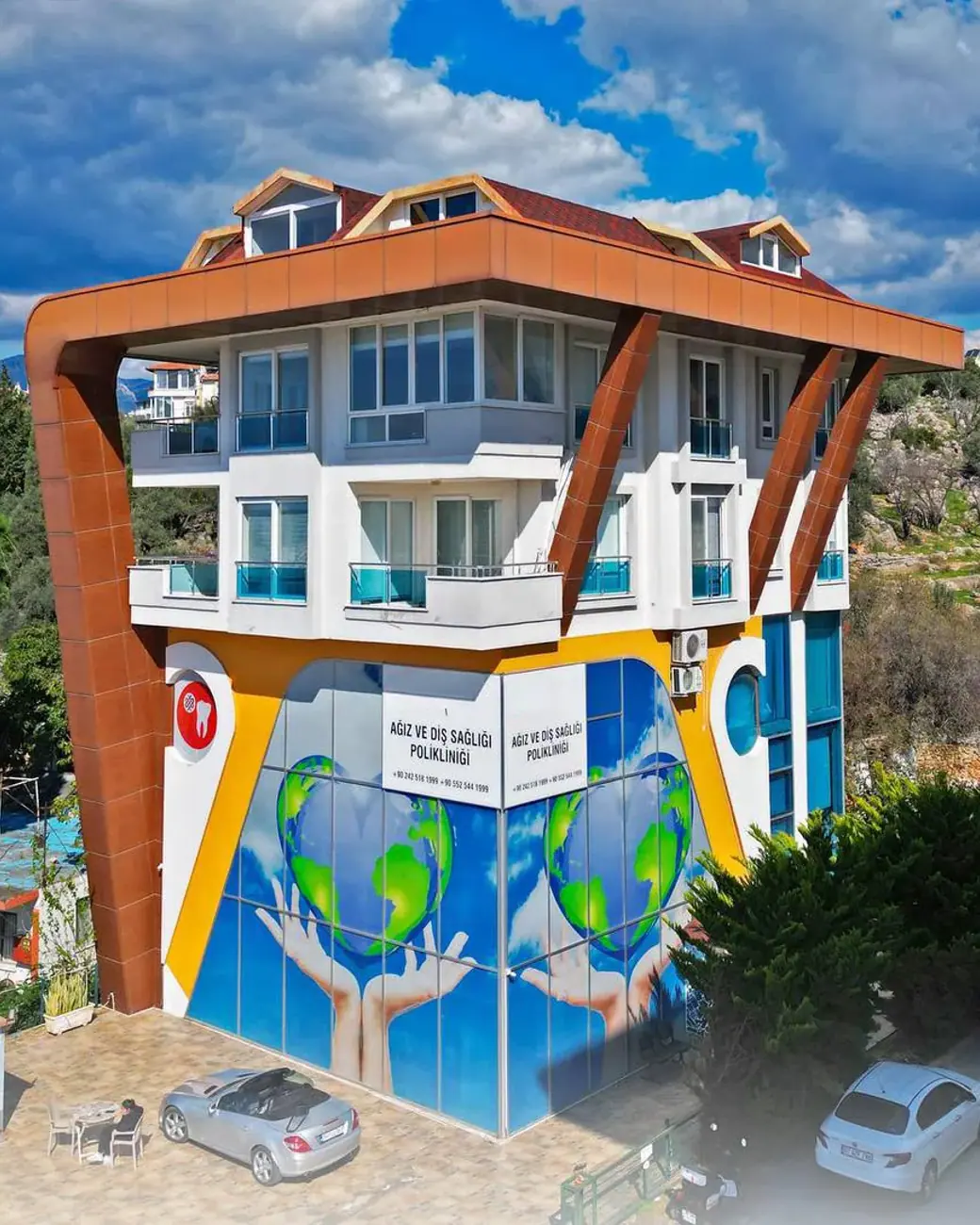 Das Gebäude von Dental Art Alanya mit bemalter Fassade und Balkonen, zwischen Bäumen am Fuß der Hügel