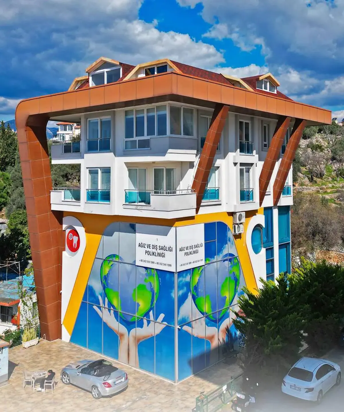 Das Gebäude von Dental Art Alanya zwischen Bäumen am Fuß der Hügel