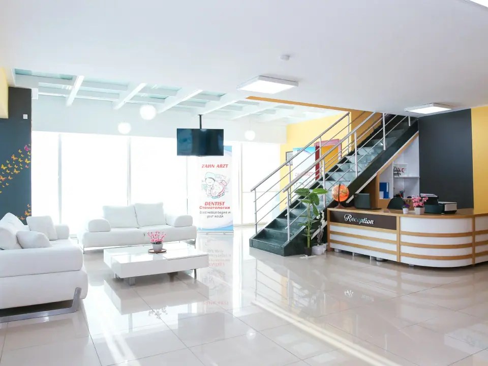 Der Empfangsbereich von Dental Art Alanya mit weißen Sofas und einer Treppe