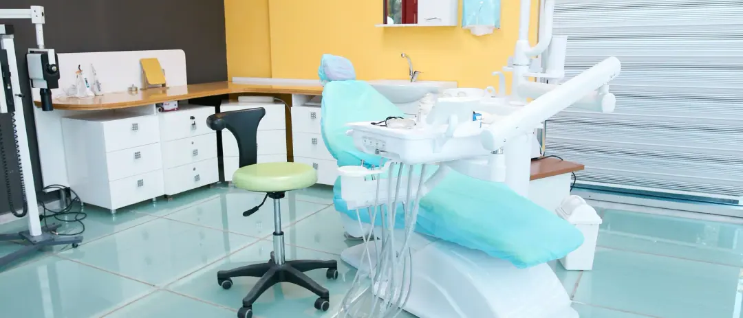 Ein heller Behandlungsraum bei Dental Art Alanya mit türkisfarbenem Behandlungsstuhl und Jalousien