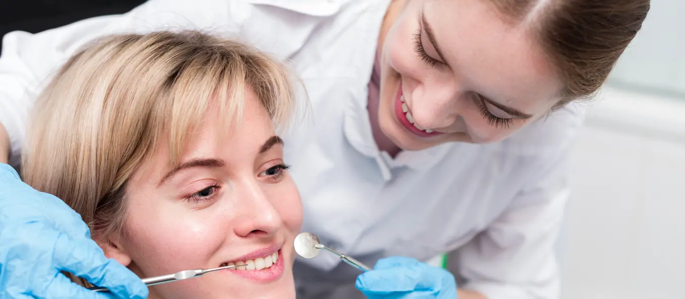 Ein Zahnarzt und eine Assistentin lächeln während einer Untersuchung gemeinsam mit einer Patientin