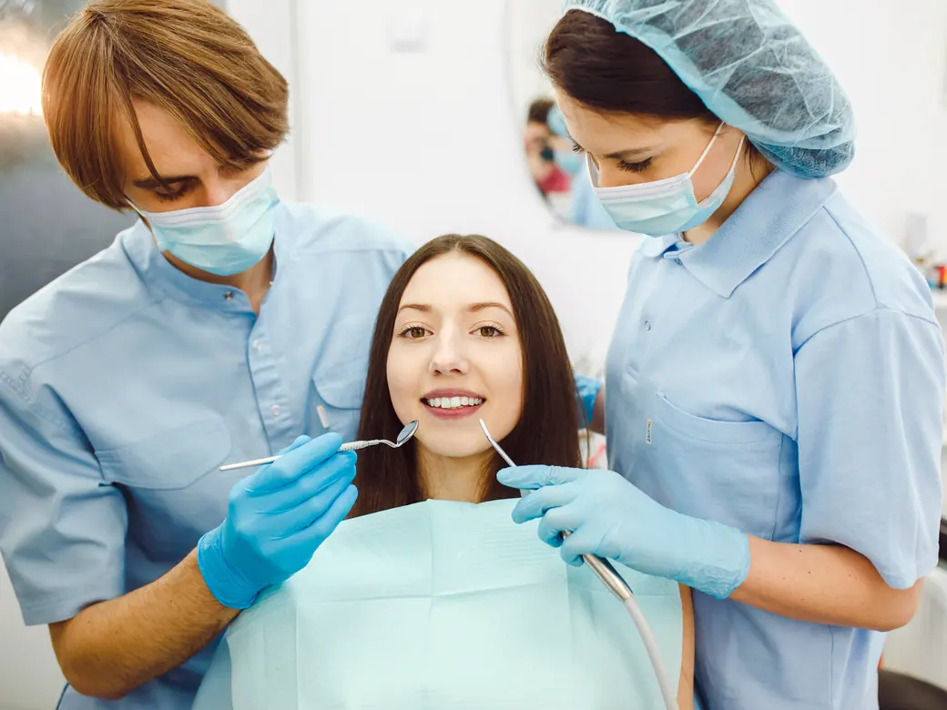 Ein Zahnarzt und eine Assistentin arbeiten zu beiden Seiten einer Patientin auf dem Stuhl