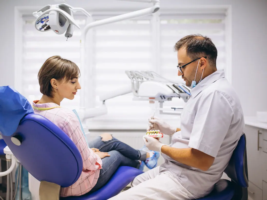 Ein Zahnarzt zeigt einer Patientin im Behandlungsraum ein Zahnmodell