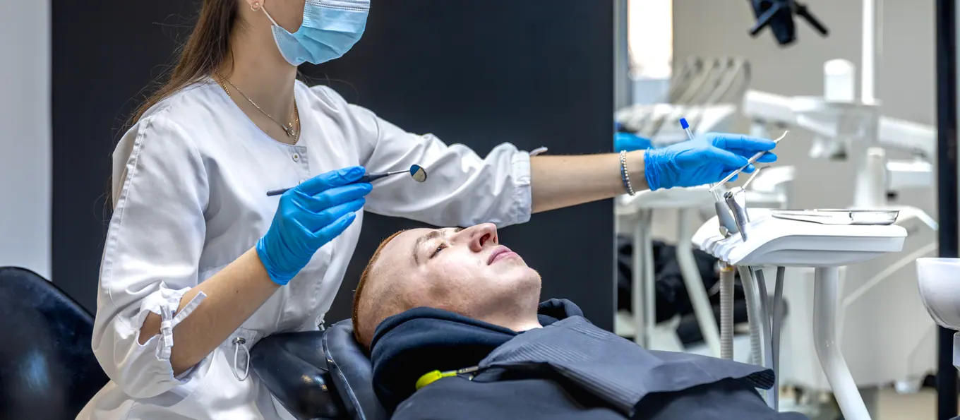 Eine Fachkraft arbeitet an einem zurückgelehnten Patienten, daneben das Instrumententablett