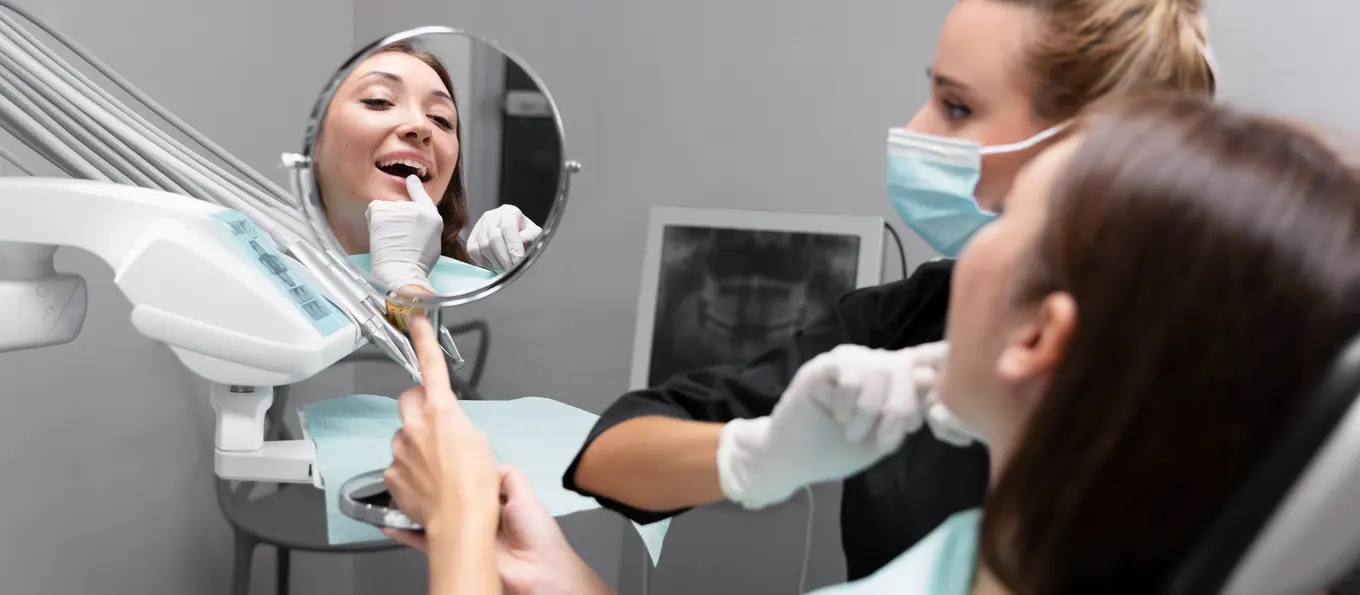 Eine Patientin betrachtet ihre Zähne in einem Handspiegel neben dem Stuhl