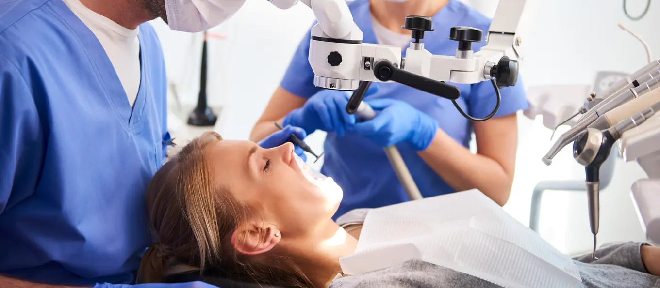Zwei Fachkräfte arbeiten an einem Dentalmikroskop an einer zurückgelehnten Patientin
