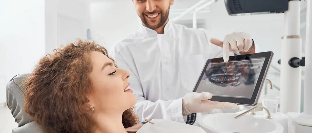 Ein Zahnarzt zeigt einer lächelnden Patientin ein Röntgenbild auf einem Tablet