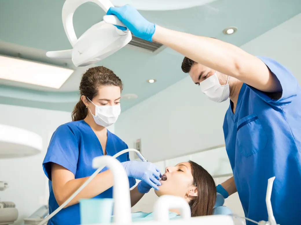 Zwei Fachkräfte arbeiten gemeinsam unter der Behandlungsleuchte an einer Patientin