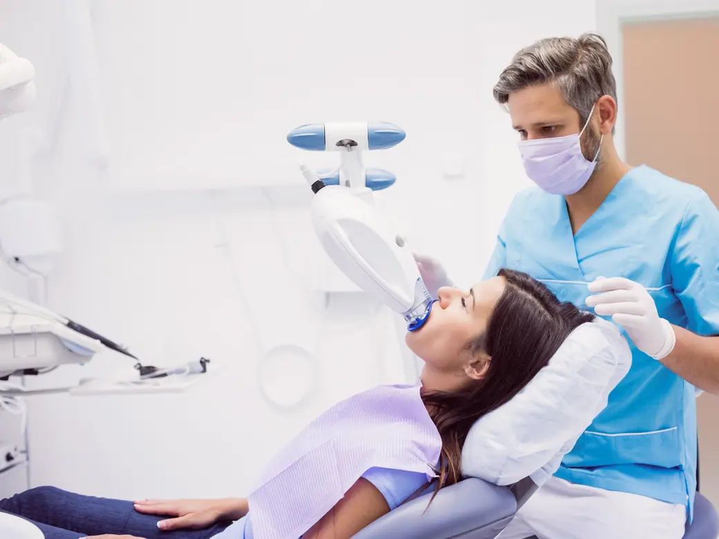 Ein Behandlungsraum mit einer Patientin unter der Behandlungsleuchte und einer Fachkraft neben dem Stuhl