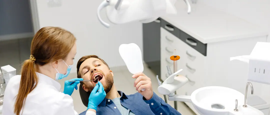 Eine Zahnärztin behandelt einen Patienten auf dem Behandlungsstuhl, während eine Assistentin zuschaut