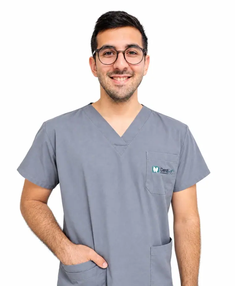 Oğuz Ulutaş, Zahnarzt bei Dental Art Alanya, lächelnd mit Brille und in der grauen Praxiskleidung der Klinik
